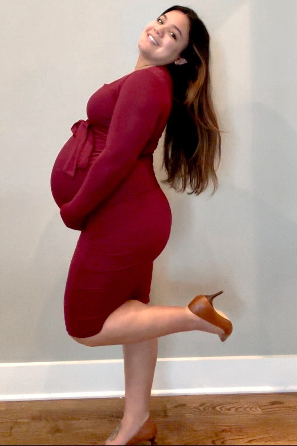 woman wearing a maternity burgundy long sleeve dress with a tie waist and showing her baby bump