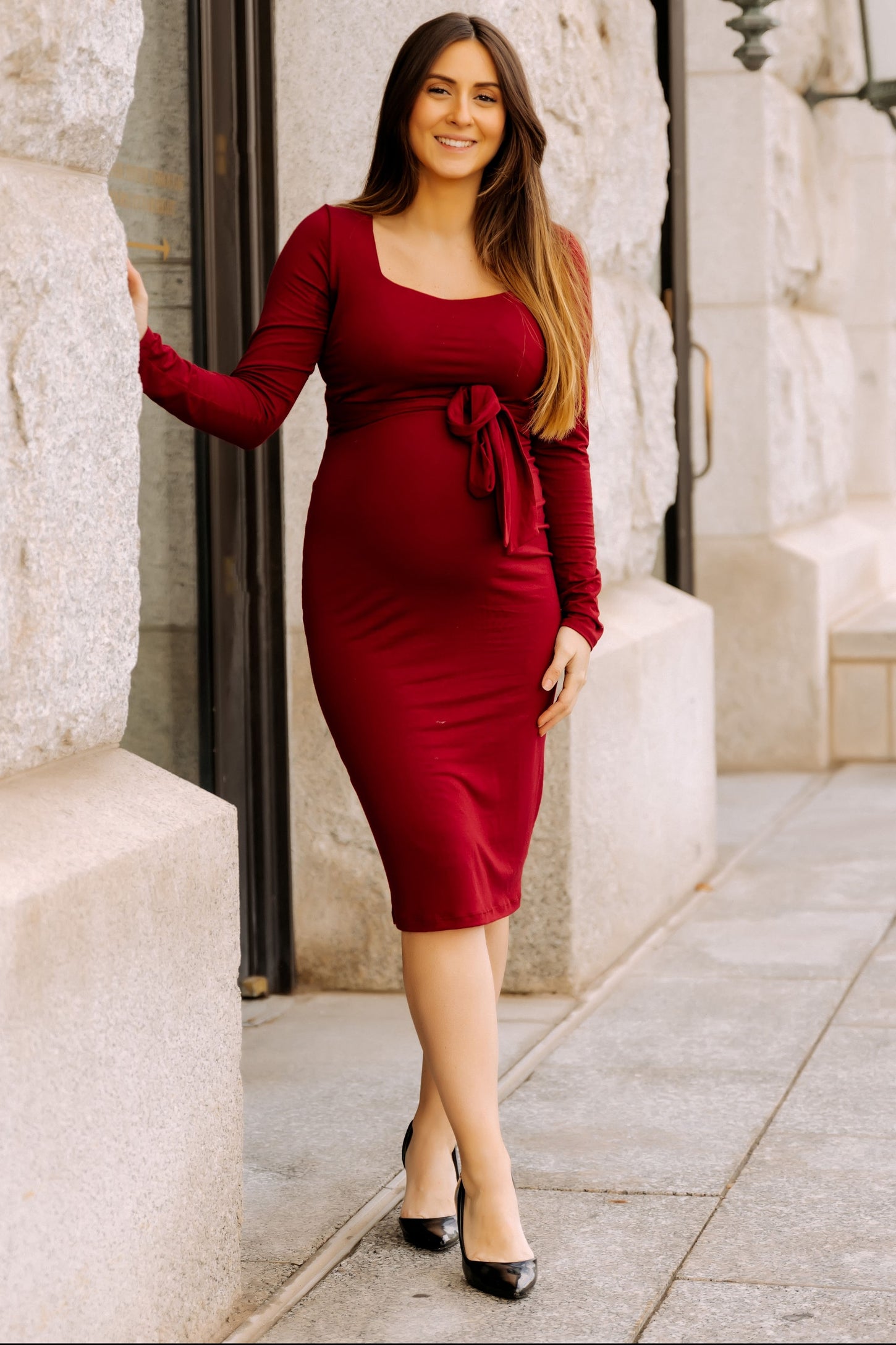 woman wearing a burgundy long sleeve maternity dress with a tie waist and a visible baby bump