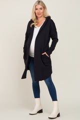woman wearing a black maternity cardigan with pockets and a white top, showing her baby bump, paired with blue jeans and white boots