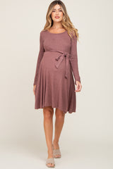 woman wearing a mauve long sleeve maternity dress with a tie waist and flared skirt, showcasing her baby bump
