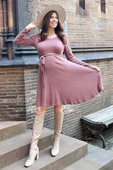 woman wearing a mauve long sleeve ribbed maternity dress with a tie waist and tall beige boots, showcasing her baby bump