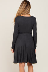 woman wearing a dark gray long sleeve maternity dress with a fitted bodice and flared skirt