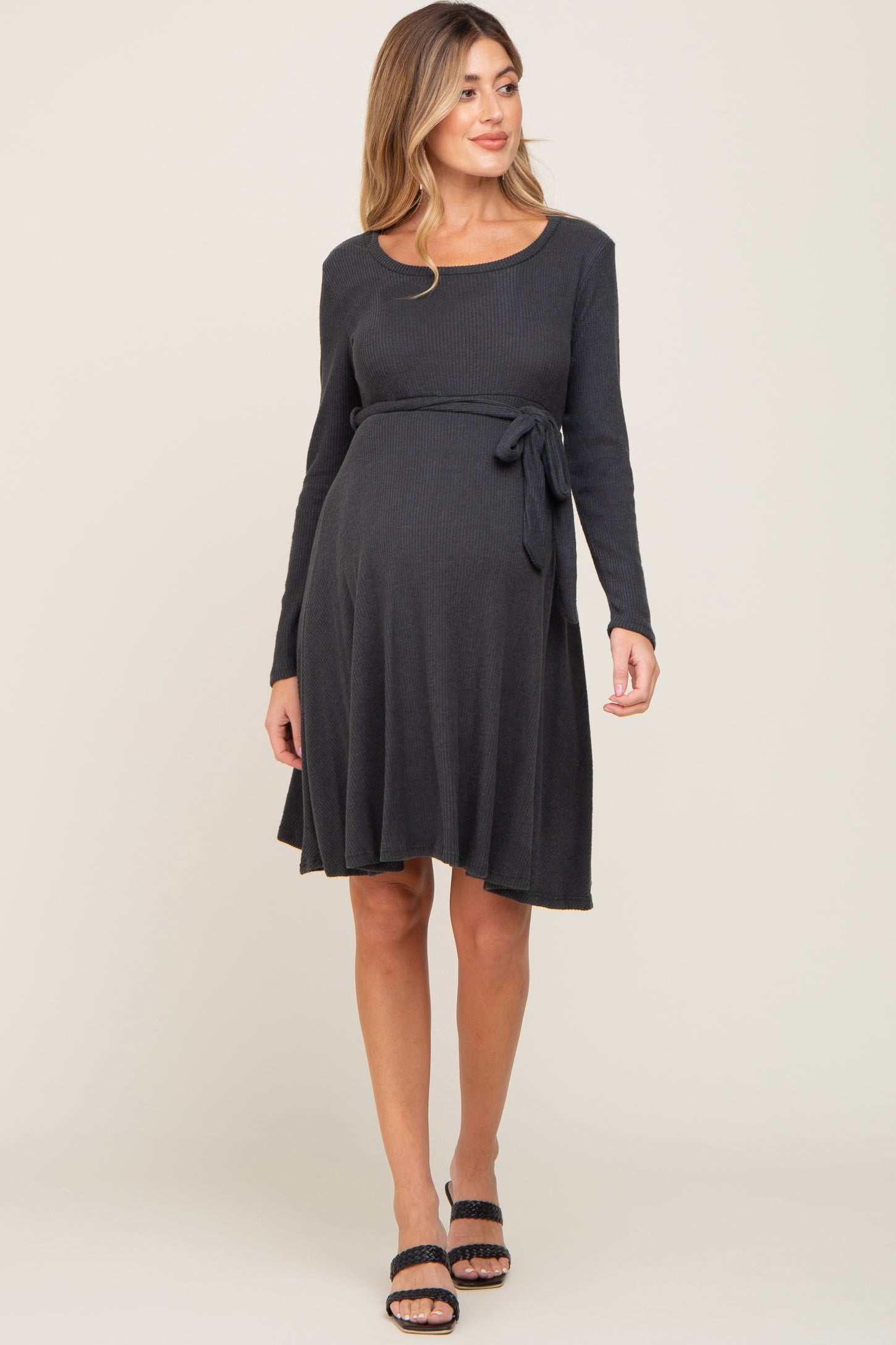 woman wearing a dark gray long sleeve maternity dress with a tie waist and a visible baby bump