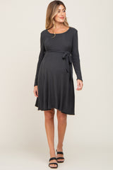 woman wearing a dark gray long sleeve maternity dress with a tie waist and a visible baby bump