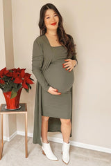 pregnant woman in olive green maternity dress and cardigan standing next to a red poinsettia plant