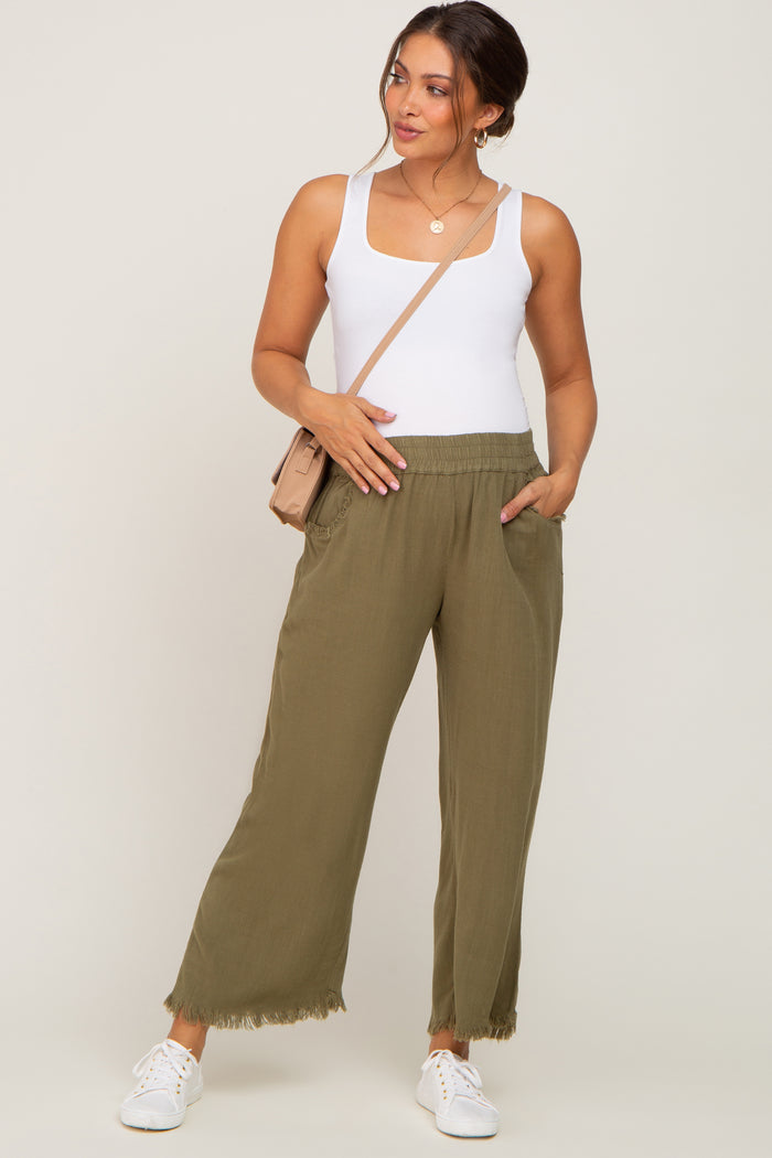 woman wearing olive green wide-leg maternity pants with pockets and a white fitted tank top, holding her baby bump