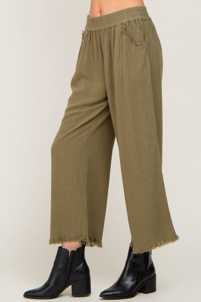 woman wearing olive green wide-leg pants with frayed hem and elastic waistband, paired with black ankle boots