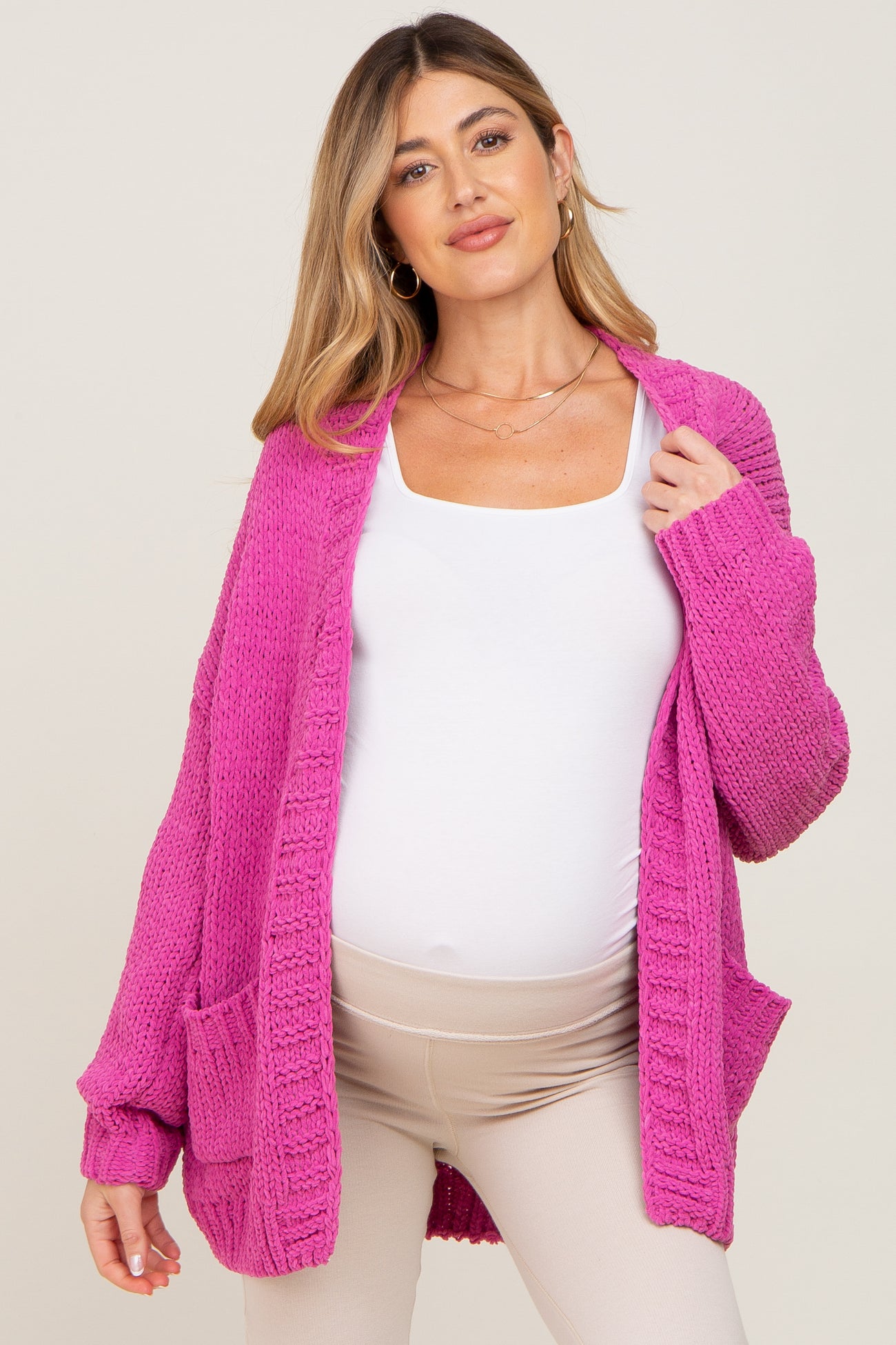 pregnant woman wearing a bright pink chunky knit maternity cardigan over a white top and beige leggings