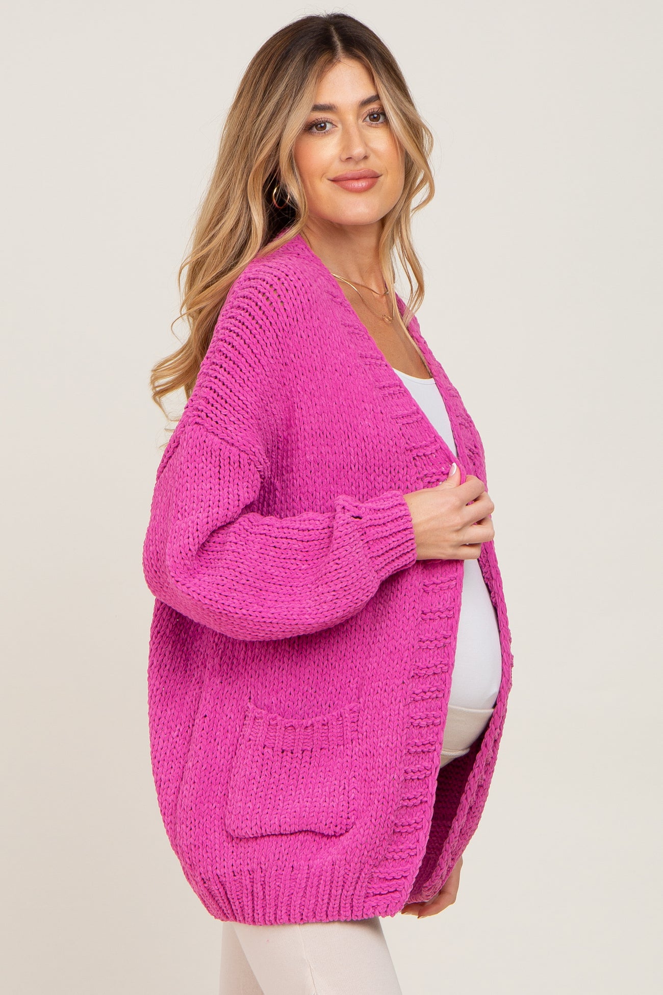 woman wearing a bright pink oversized maternity cardigan with pockets and a visible baby bump