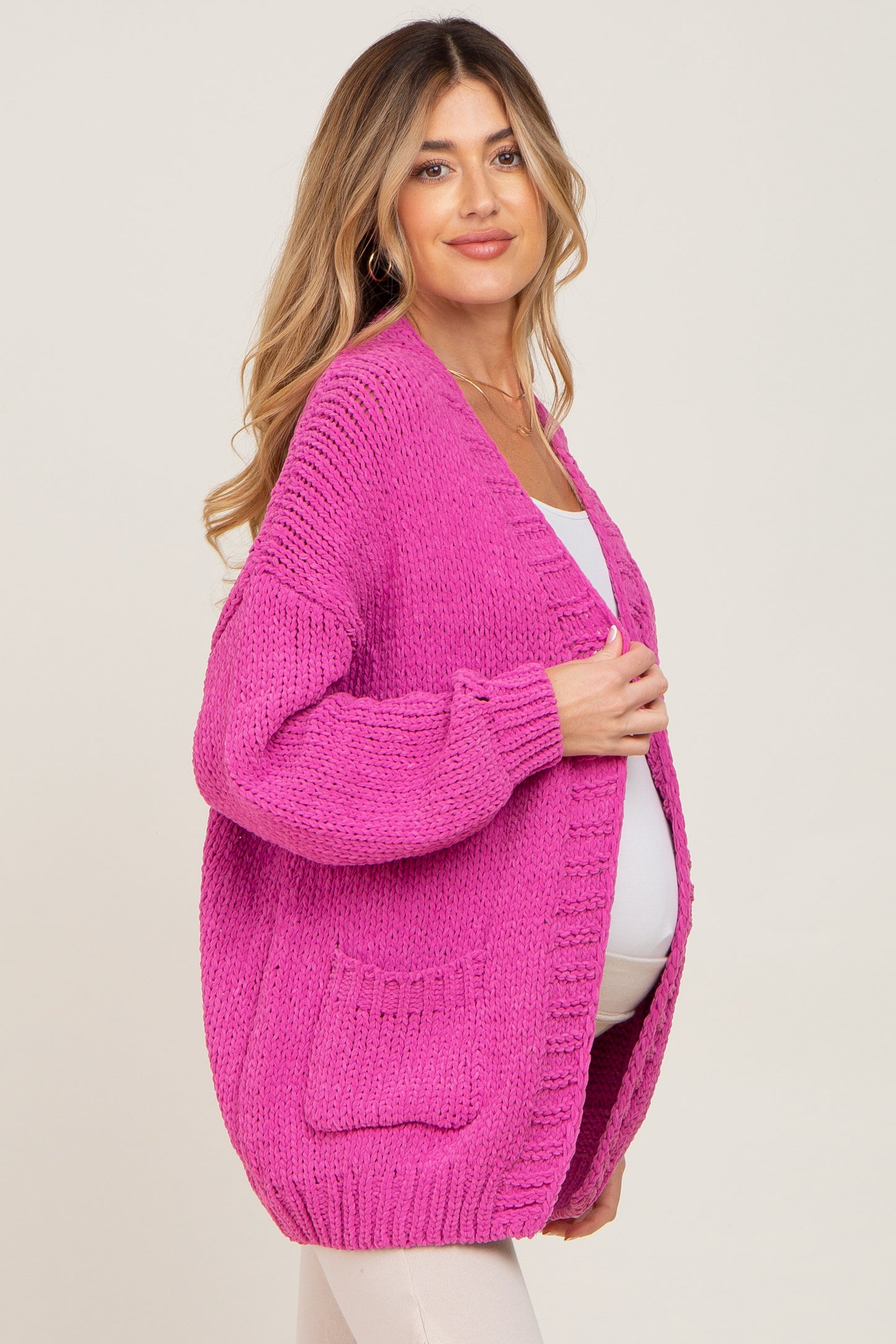 woman wearing a bright pink oversized maternity cardigan with pockets and a visible baby bump