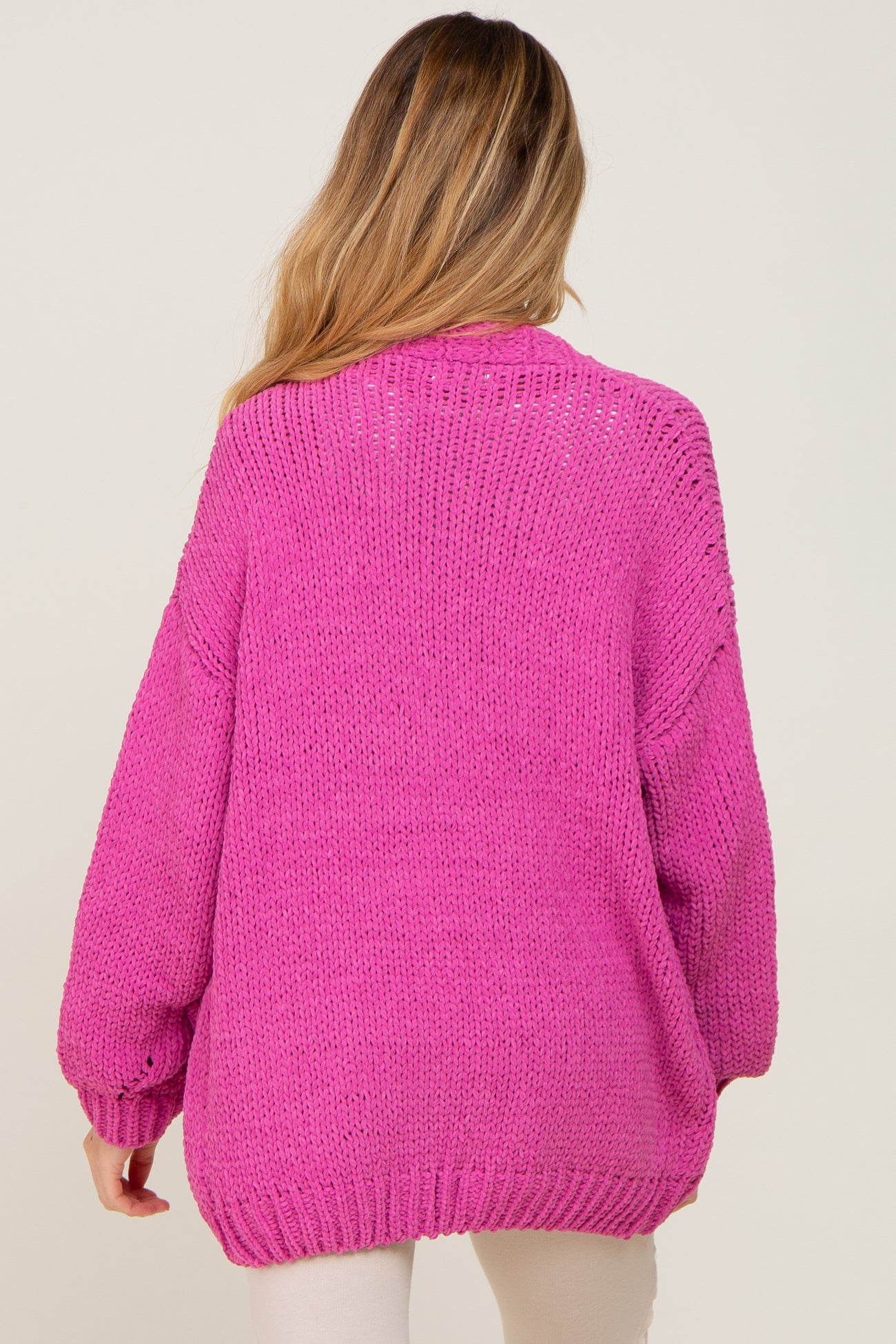 woman wearing a bright pink oversized knit maternity sweater, view from the back