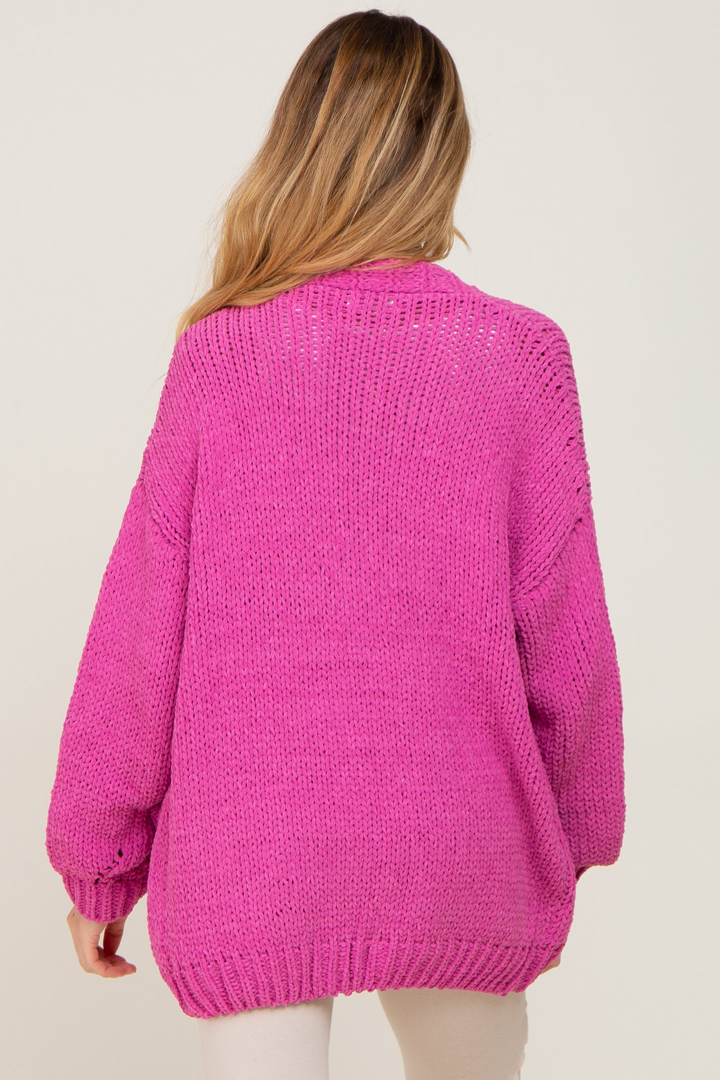 woman wearing a bright pink oversized knit maternity sweater, view from the back