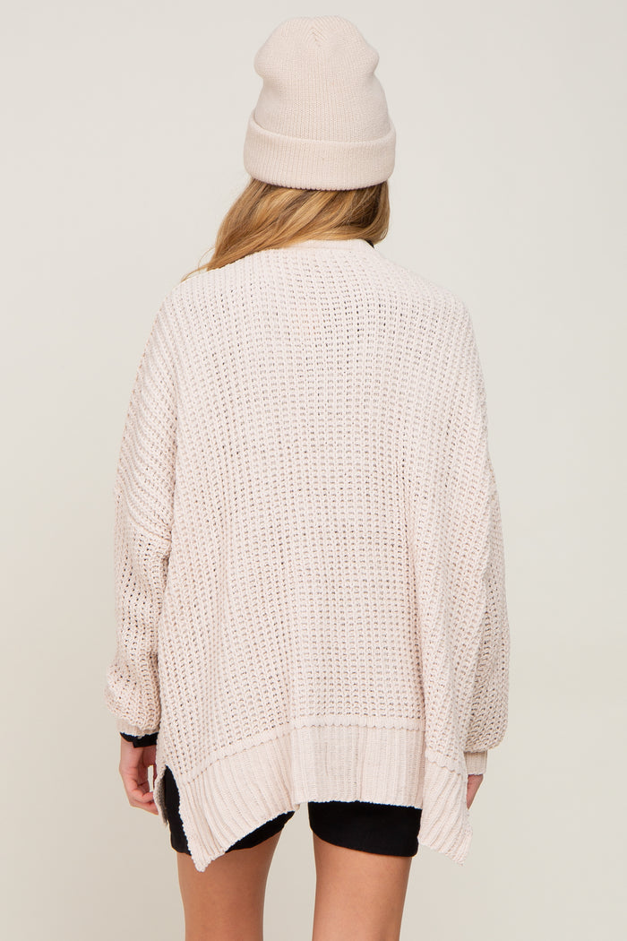 woman wearing a light pink oversized knit maternity cardigan and a matching beanie, viewed from the back