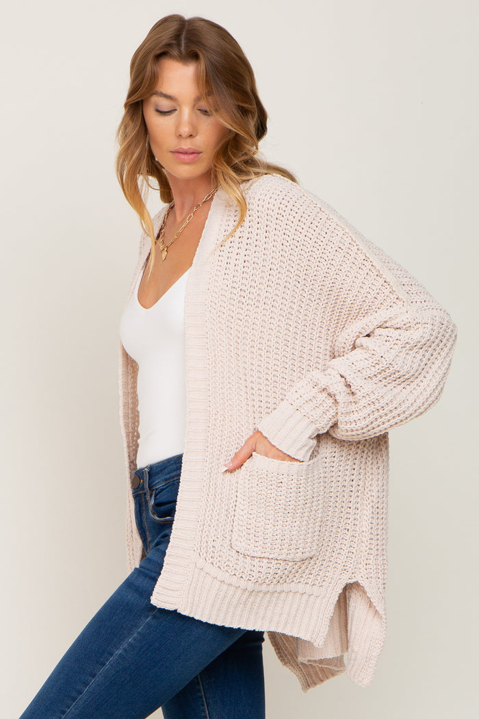 woman wearing a light pink knitted cardigan with side pockets, paired with a white top and blue jeans