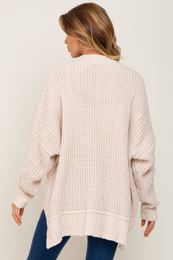 Back view of a woman wearing an oversized cream chunky knit cardigan sweater with ribbed cuffs and hem