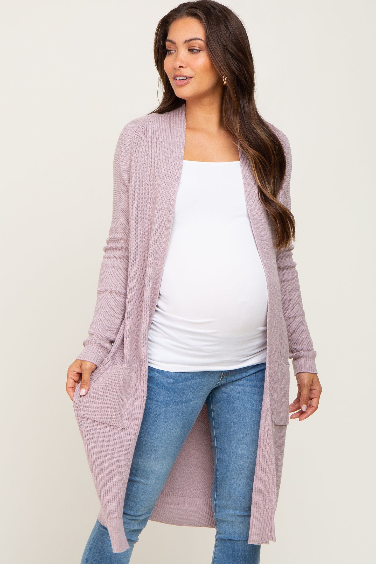 woman wearing a light lavender long sleeve maternity cardigan over a white top, showing her baby bump and paired with blue jeans