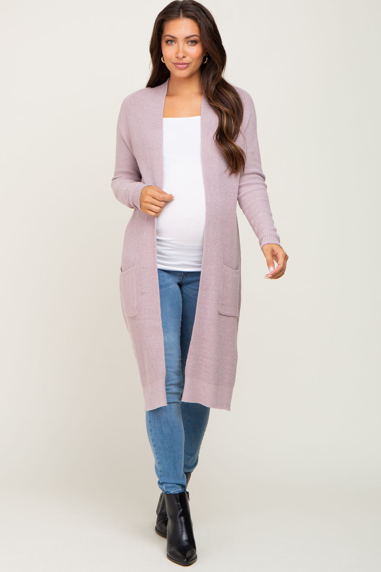 woman wearing a light pink long cardigan with pockets and a white maternity top, showing her baby bump