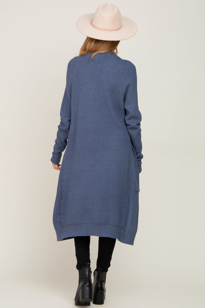 woman wearing a long blue maternity cardigan with a loose fit and side pockets, facing away from the camera