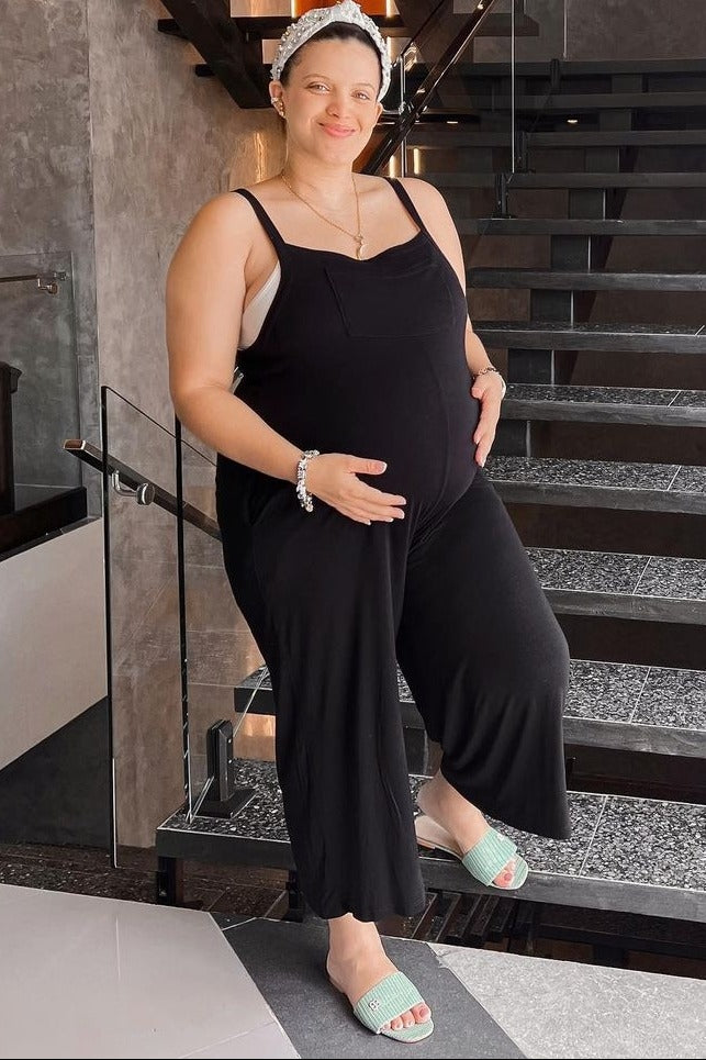 woman wearing a black maternity jumpsuit with a visible baby bump, standing on stairs