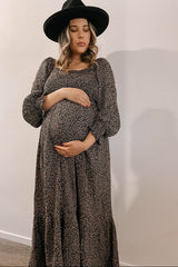 Pregnant woman in leopard print maternity dress and black wide-brim hat holding her baby bump