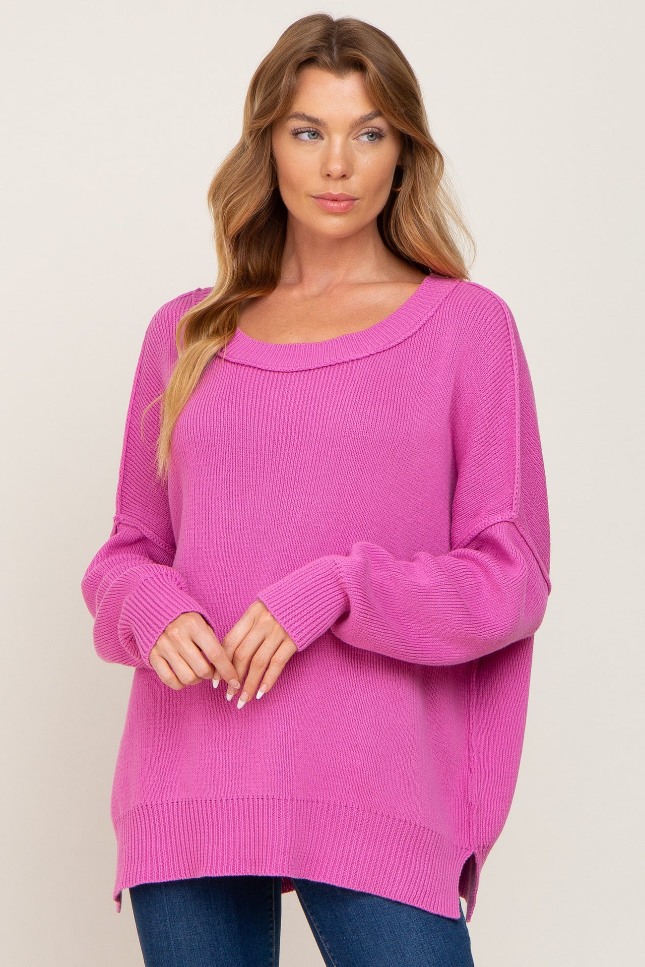 woman wearing a bright pink oversized sweater with a scoop neckline and long sleeves, paired with blue jeans
