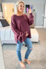 woman wearing a burgundy maternity sweater and distressed jeans, holding her baby bump while smiling in a mirror selfie