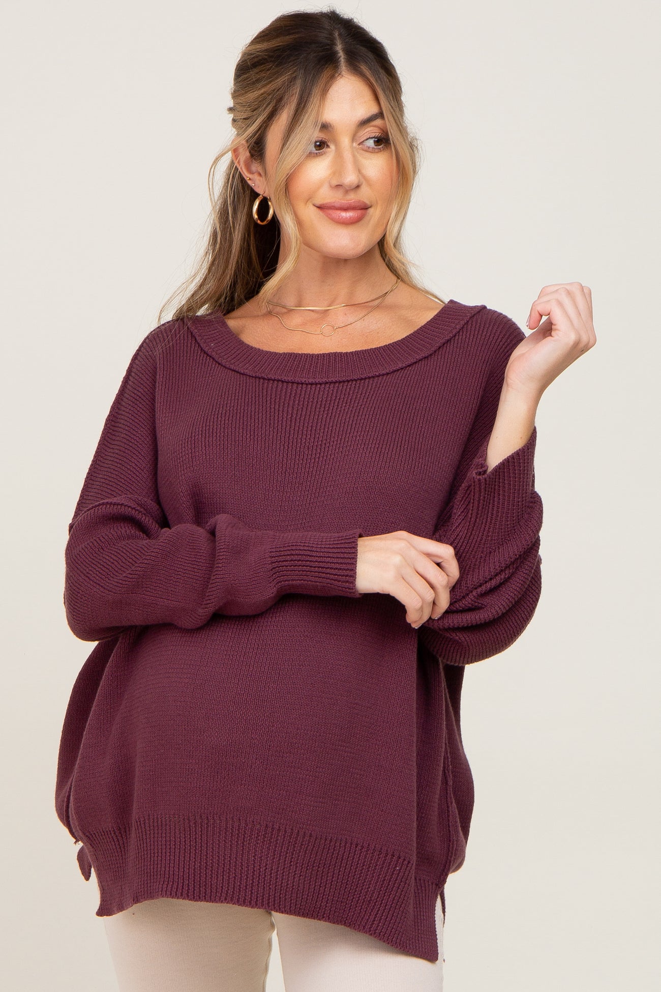 woman wearing a deep burgundy maternity sweater with a loose fit and rolled cuffs, showing a visible baby bump