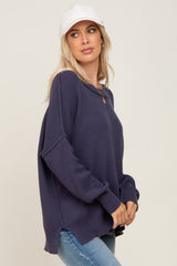 woman wearing a navy blue knitted sweater with side slits and relaxed fit, paired with light blue jeans and a white cap
