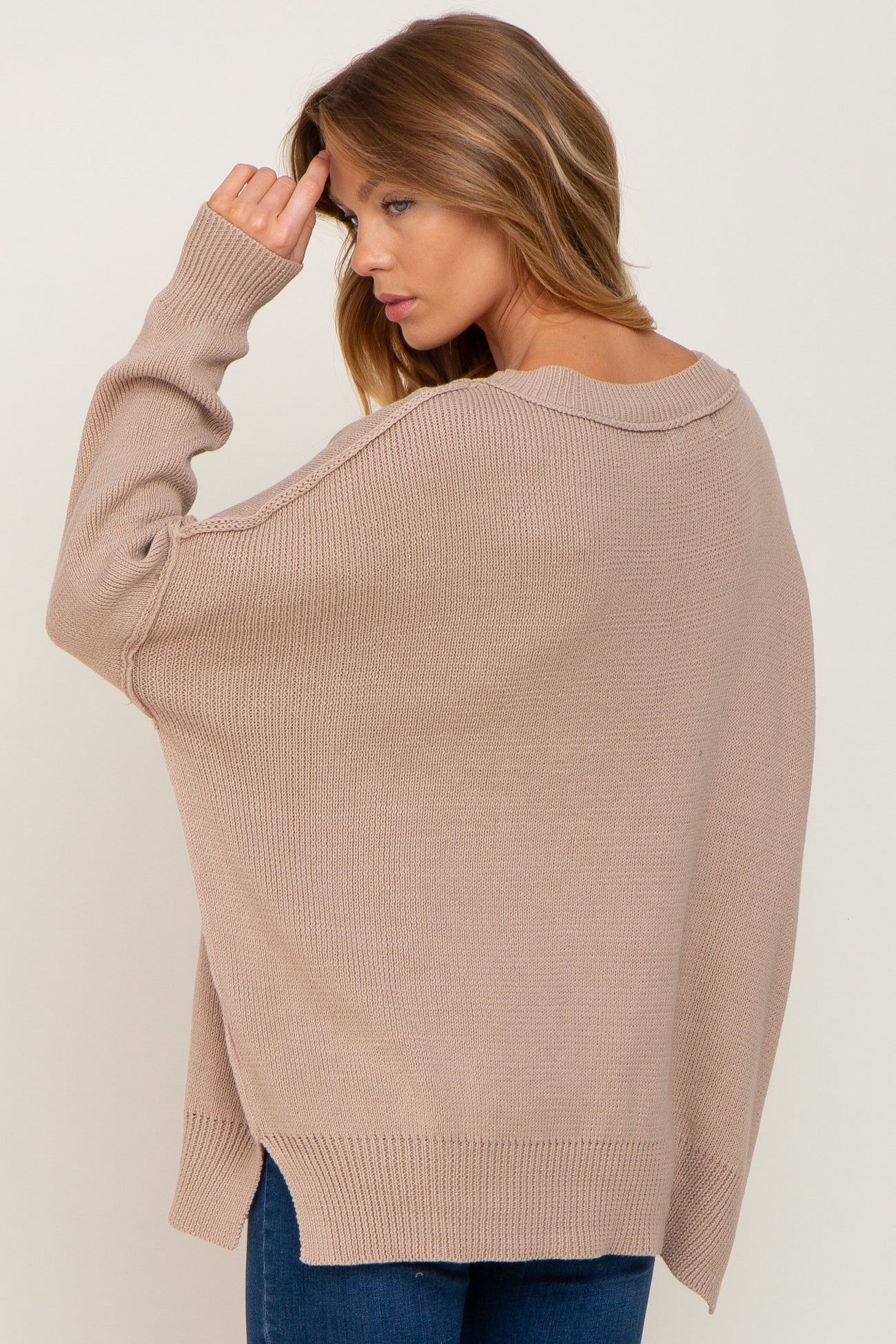 woman wearing a beige oversized sweater with a wide neckline and drop shoulders, styled with blue jeans