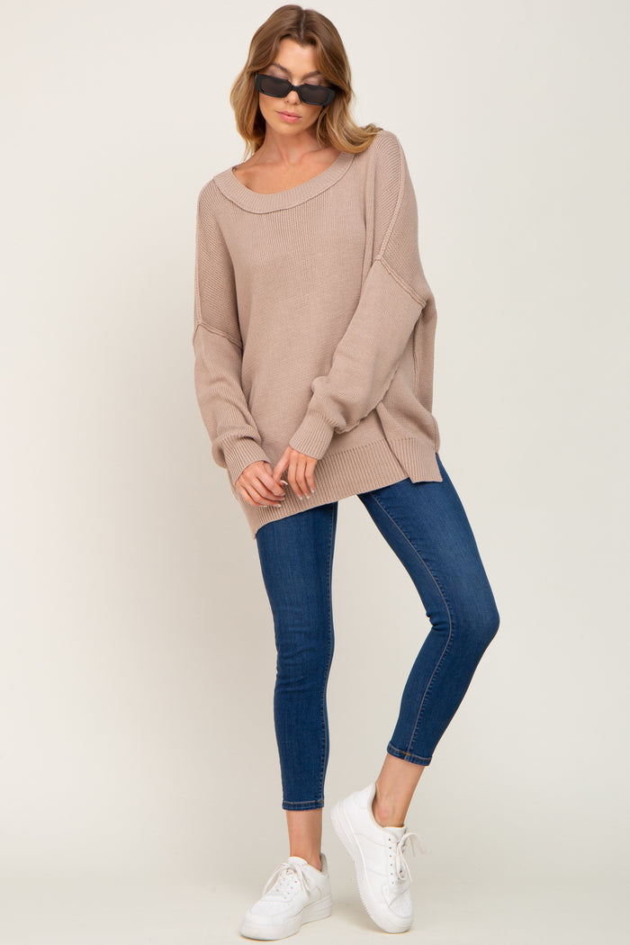 woman wearing a beige oversized sweater with long sleeves and blue skinny jeans, paired with white sneakers and sunglasses