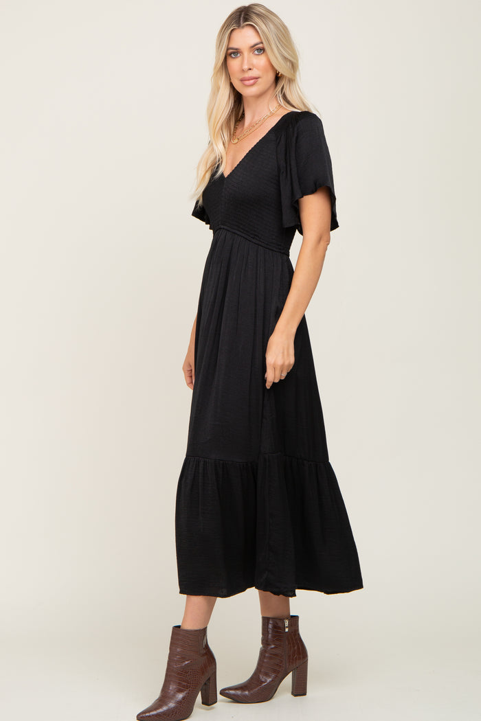 Woman wearing a black smocked midi dress with flutter sleeves and brown crocodile boots
