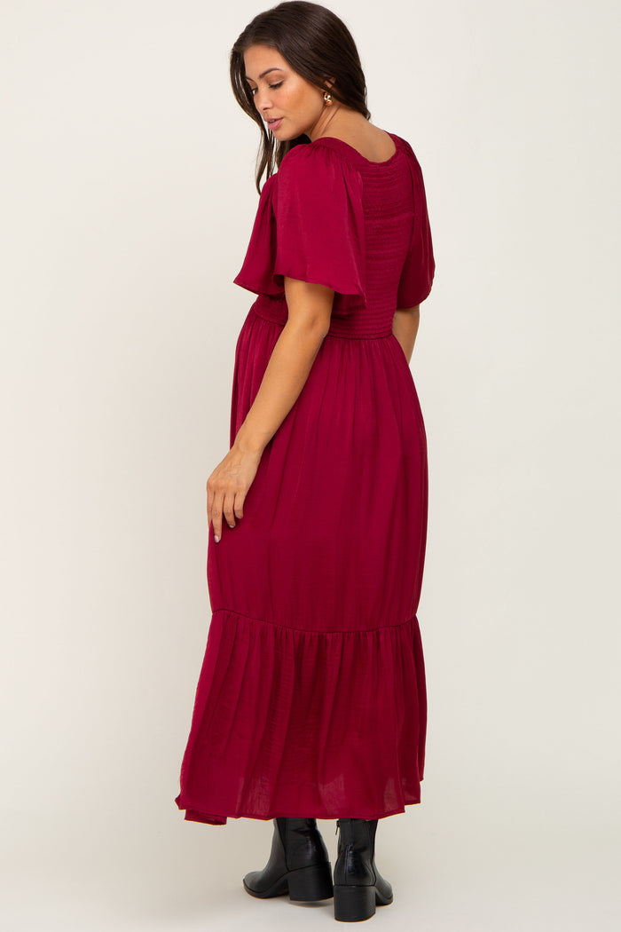 Pregnant woman in a burgundy smocked maternity maxi dress with flutter sleeves and black boots