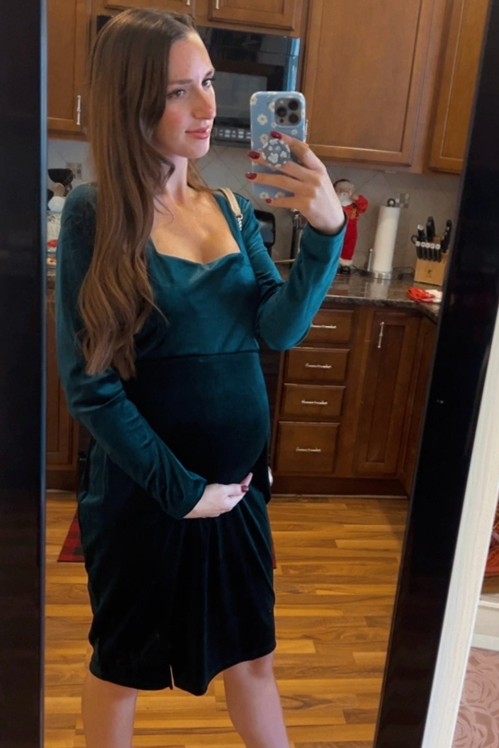woman wearing a dark green long sleeve maternity dress and cradling her baby bump in front of a mirror