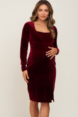 woman wearing a burgundy long sleeve velvet maternity dress and gently cradling her baby bump