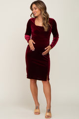 woman wearing a burgundy velvet maternity dress with long sleeves and a side slit, highlighting her baby bump