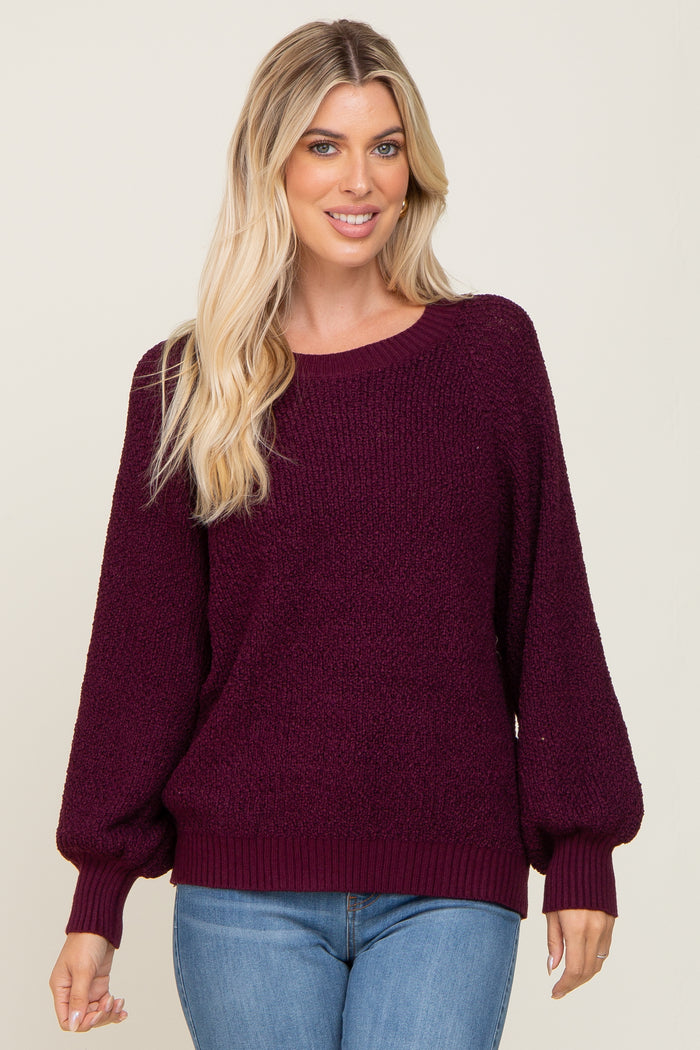 woman wearing a maroon oversized sweater with balloon sleeves and a scooped neckline, paired with blue jeans