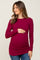 woman wearing a burgundy long sleeve maternity top with side ruching and holding her baby bump