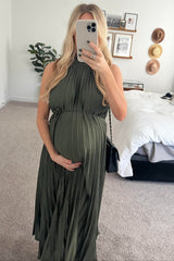 woman wearing a dark green pleated maternity dress and holding her baby bump in front of a mirror