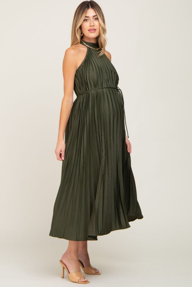 woman wearing a dark green pleated maternity dress with a halter neck and a tied waist, showing her baby bump