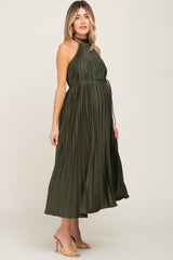 woman wearing a dark green pleated maternity dress with a halter neck and a tied waist, showing her baby bump