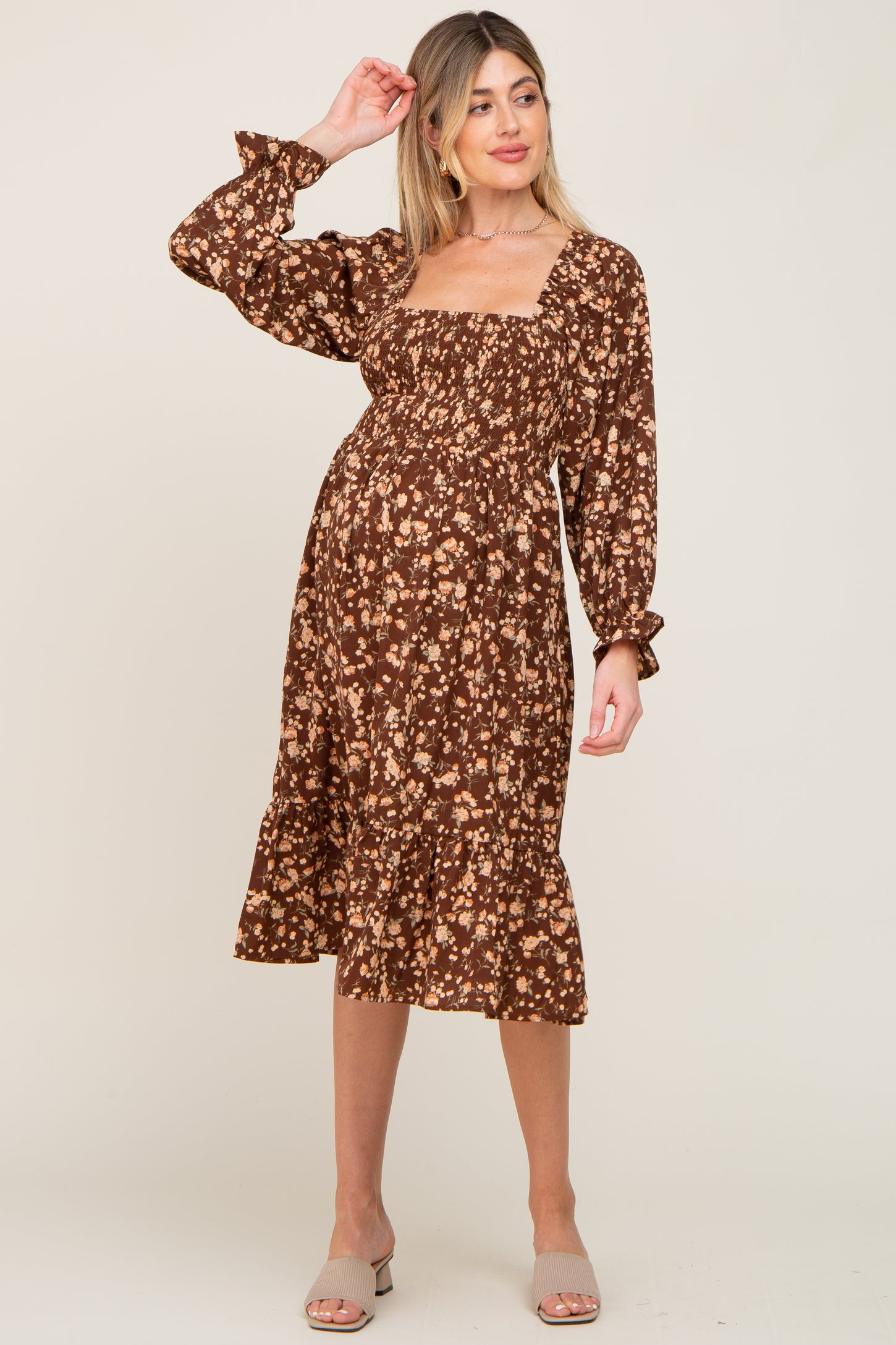 woman wearing a brown floral maternity dress with a square neckline and long sleeves, featuring a ruffled hem and a visible baby bump