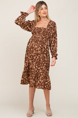 woman wearing a brown floral maternity dress with a square neckline and long sleeves, featuring a ruffled hem and a visible baby bump