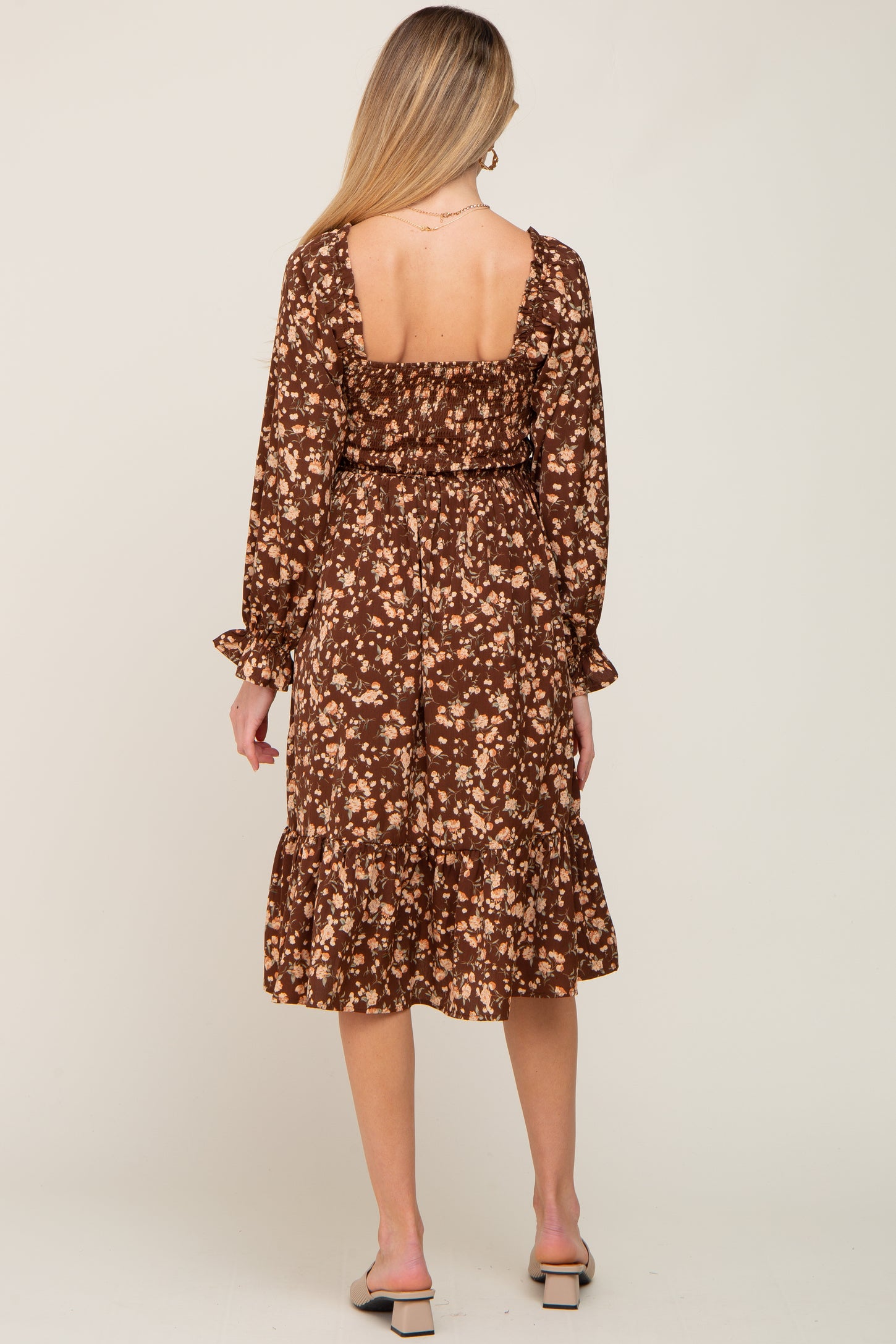 woman wearing a brown floral long sleeve maternity dress with a fitted bodice and ruffled hem