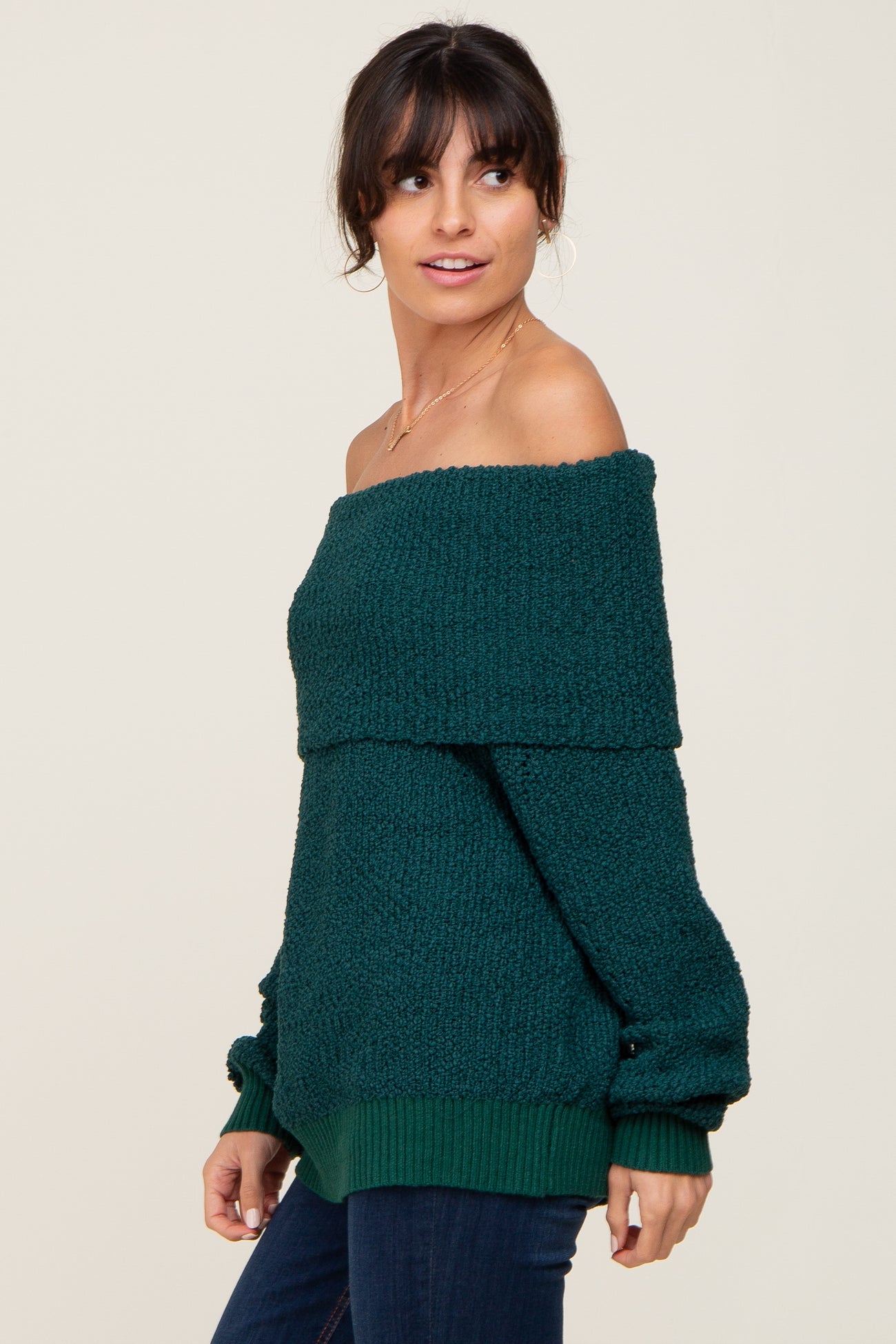 woman wearing a dark teal off-the-shoulder knit sweater with long sleeves and ribbed hem, styled casually with jeans