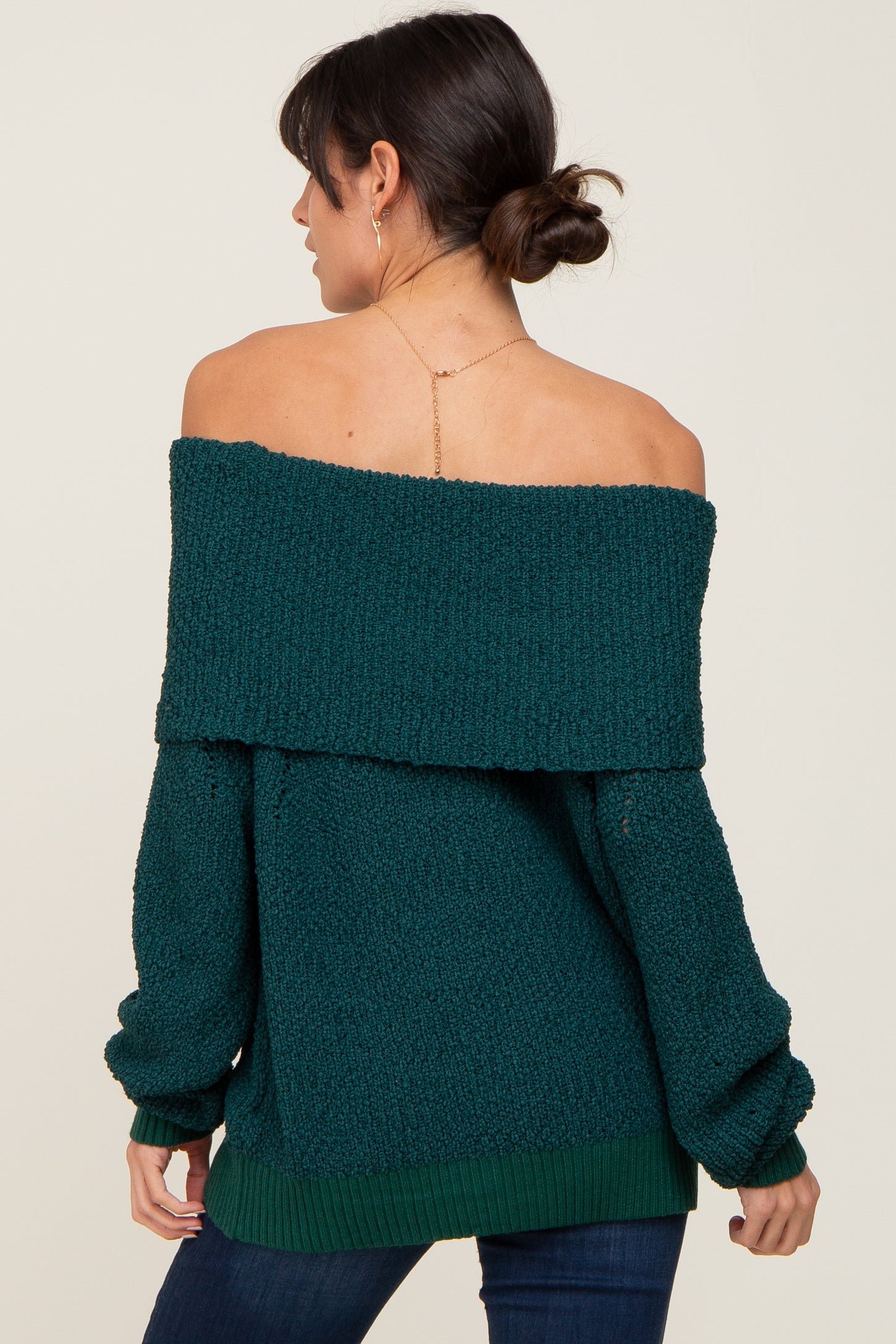 Woman wearing a dark green off-the-shoulder knit sweater with a fold-over neckline and long sleeves
