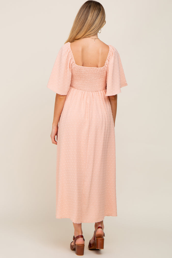 woman wearing a pale pink maternity maxi dress with short flutter sleeves and a smocked waist from the back