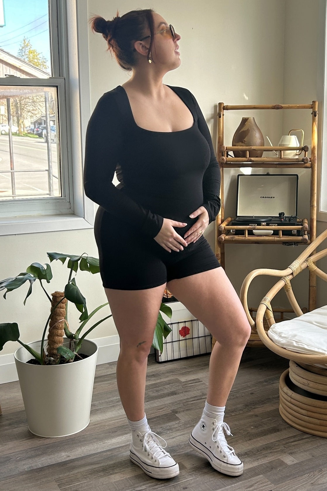 woman wearing a black long sleeve maternity bodysuit and black shorts, holding her baby bump