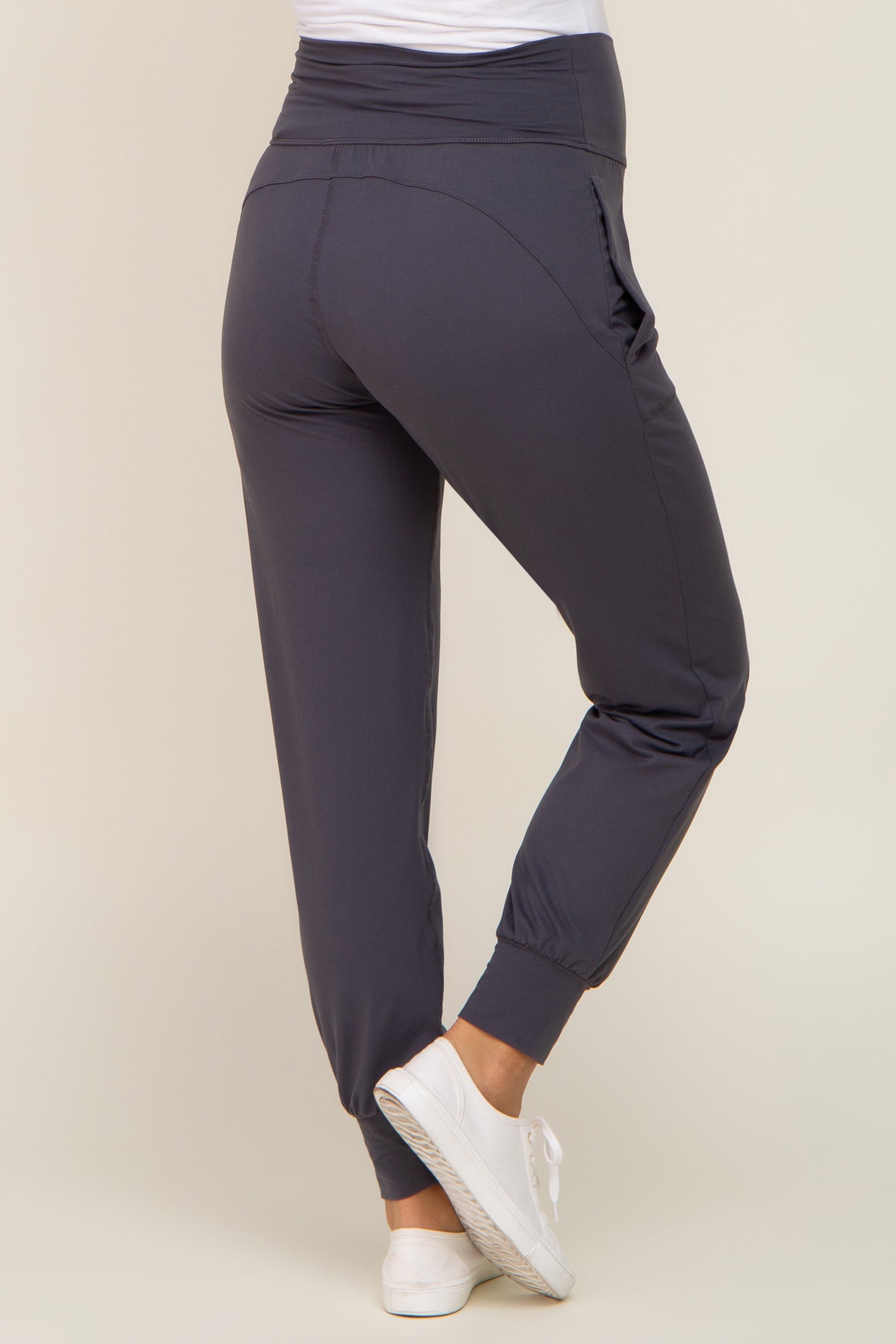 woman wearing dark grey maternity joggers with a high waistband and elastic cuffs, standing sideways with a slight turn