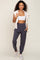 woman wearing a white sports bra and gray jogger pants with pockets, styled with a light beige vest