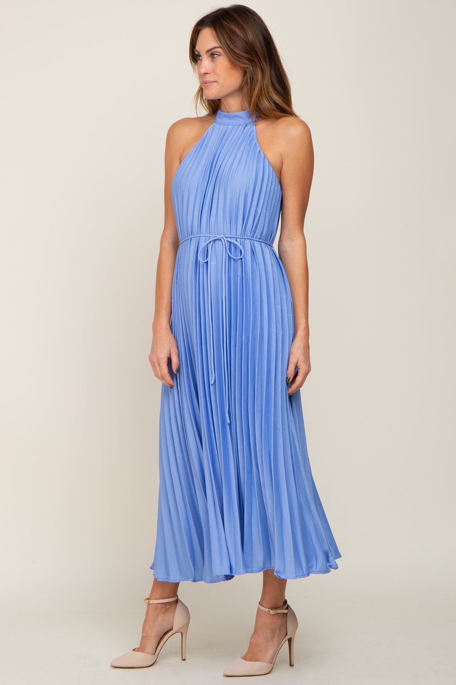 woman wearing a light blue pleated halter neck midi dress styled with a tie waist detail and beige heels